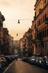 Cars parked on city street amidst buildings against sky during sunset