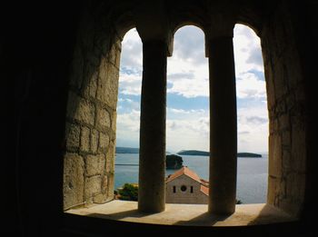 Built structure by sea against sky seen through window