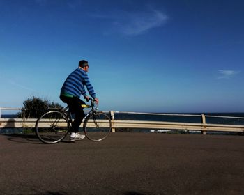 Man riding bicycle on road against clear blue sky