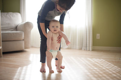 Sister helping brother to walk on floor at home