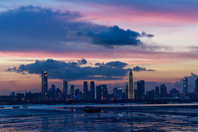 Sea by buildings against sky during sunset