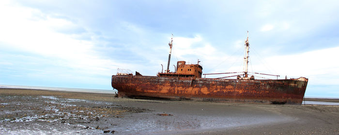 Abandoned ship moored on beach against sky