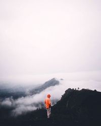 Rear view of man standing on mountain against sky