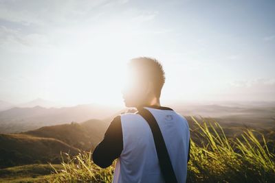 Rear view of woman standing on field against sky during sunset