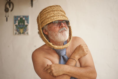 Shirtless man wearing basket on head while gesturing against wall