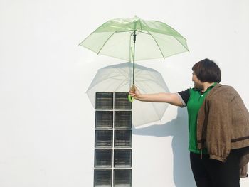 Woman holding umbrella while standing by wall