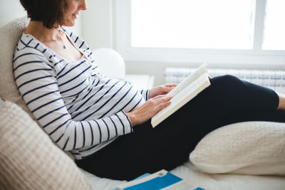 Midsection of woman reading book at home