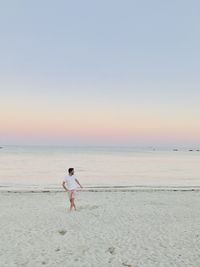 Rear view of woman walking at beach against clear sky