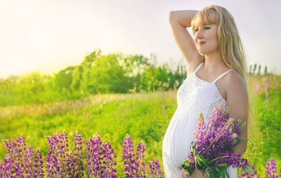 Pregnant woman with flowers standing in field