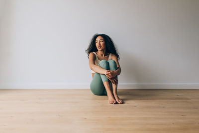 Beautiful multiracial sporty woman in sportswear sitting on the floor