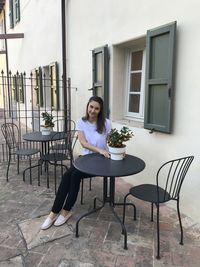 Full length of woman sitting at table by building