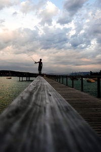 Boy fishing while standing on jetty by boats and river