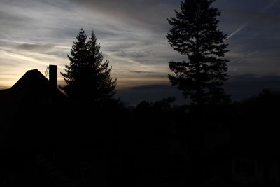 Silhouette trees by house against sky during sunset