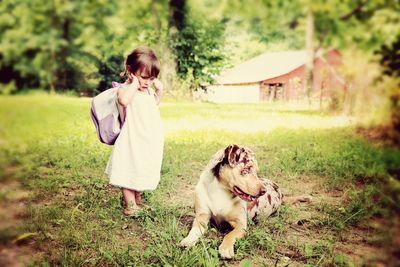 Full length of girl looking at dog relaxing on grassy field