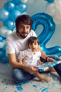 Father and son open a gift for the child's birthday on the background of blue balloons