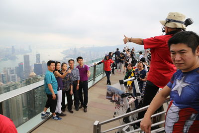 People standing by railing against sky in city