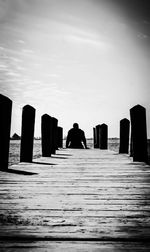 Rear view of man sitting on wooden pier