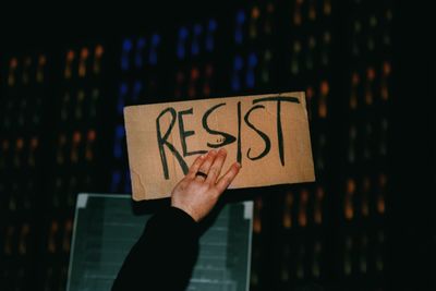 Cropped hand of person holding resist text on cardboard