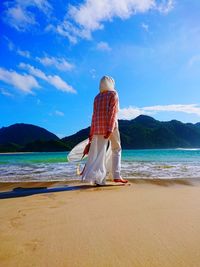Rear view of woman standing on beach against sky