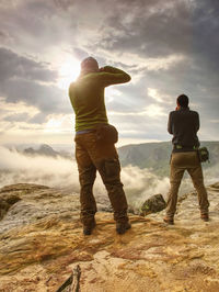 Hiker and photographer with camera stay on cliff and takes photos. autumn nature, misty landscape 