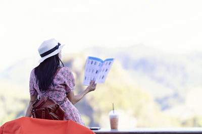 Rear view of woman holding umbrella against sky