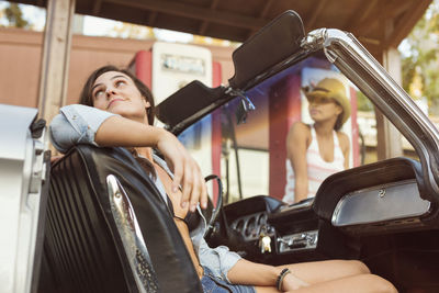 Woman sitting in car while friend standing at fuel pump