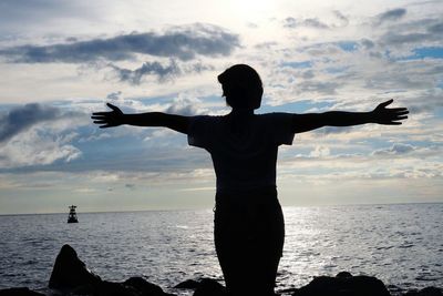 Rear view of silhouette woman with arms outstretched standing in front of sea