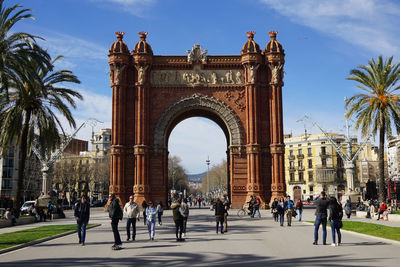 People walking on street by arc de triomf against sky