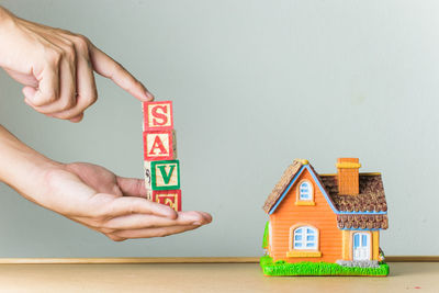 Close-up of hands holding text by model house against gray background