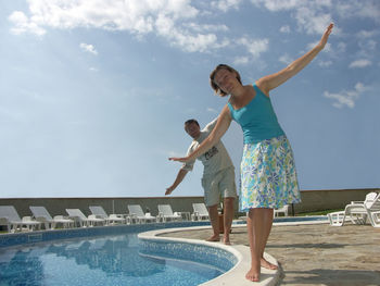 Woman standing by swimming pool against sky