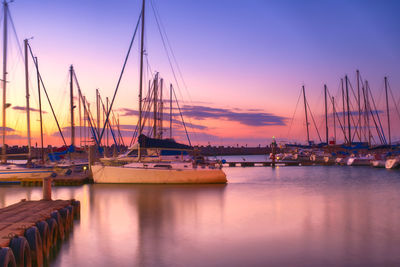 Boats moored in harbor at sunset