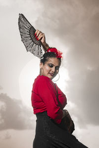 Portrait of woman with leaf fan standing against sky