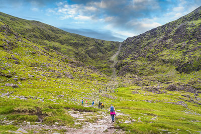 Rear view of people climbing hill against sky