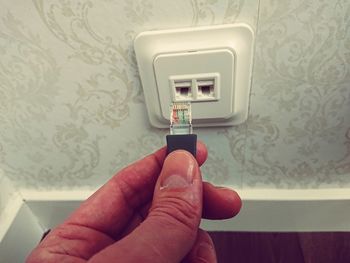 Close-up of hand holding network connection plug against wall