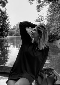 Smiling young woman sitting by lake against sky