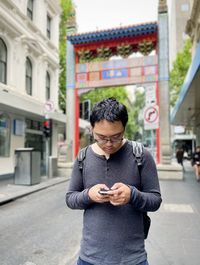 Portrait of asian man using smart phone against arch and buildings in chinatown-melbourne australia.