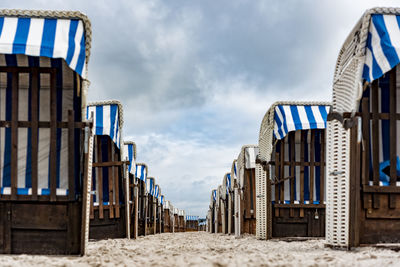 Hooded beach chairs in row on sand against cloudy sky