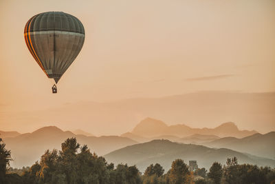 Hot air balloon flying over mountains against sky during sunset