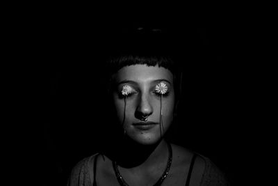 Close-up of young woman with flowers on eyes against black background