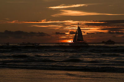 Silhouette of sailboat in sea during sunset