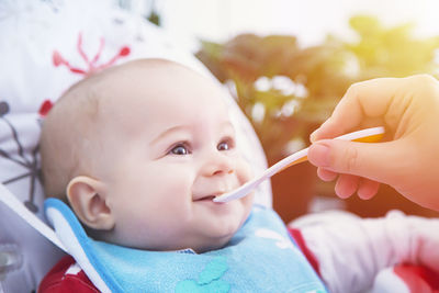 Cropped hand feeding cute baby boy from spoon outdoors