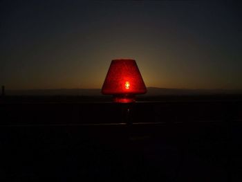 Illuminated red light bulb against sky at sunset