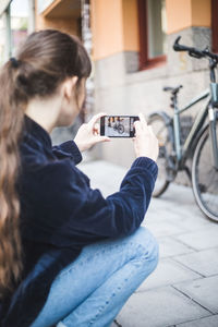 Young woman photographing bicycle on footpath