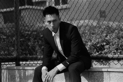 Portrait of young man sitting against chainlink fence