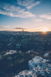 Man standing on rock against cityscape during sunset