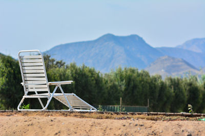 Empty chair on landscape against sky