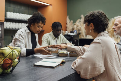 Businesswoman giving lunch boxes to colleagues sitting at table