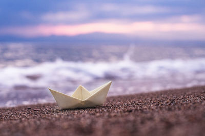 Close-up of paper ship floating on beach against sky during sunset