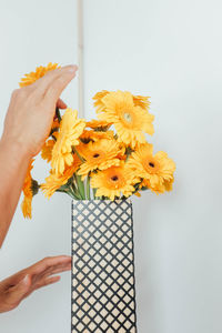 Close-up of hand holding yellow flower vase against white background