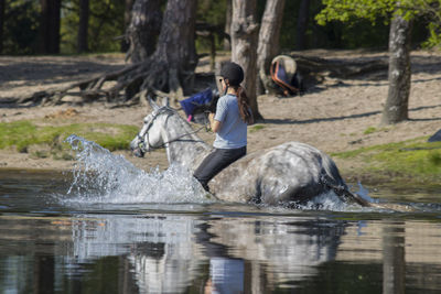 Woman riding horse in lake at forest